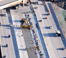 GOMACO paving train slipforming next to concrete covered with blankets and plastic.