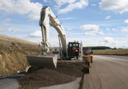 Excavator spreading concrete on road