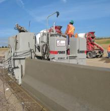 Concrete slipformer installing a barrier