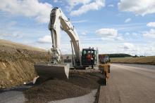 Excavator spreading concrete on road