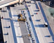 GOMACO paving train slipforming next to concrete covered with blankets and plastic.